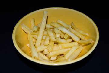delicious and crisp french fries, potato, in yellow ceramic bowl, isolated on black background