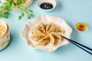 Gyoza dumplings with duck cooked in bamboo steamer served on a plate with soy sauce, sesame seeds and cilantro. Top view, blue background