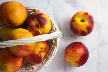 White basket with fresh nectarines on white marble, top view