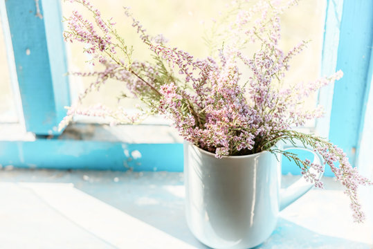 Heather flowers in a cup on  an old wooden window in a farmhouse.. Vintage retro style.

