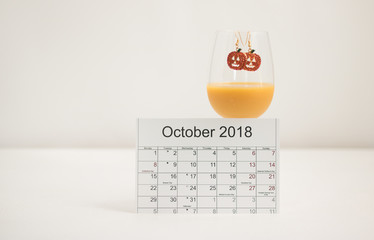 Calendar October 2018 and a glass of fresh juice, decorated fashionable earrings with an image of orange pumpkin Halloween on a white background. Concept: fashionable & fun autumn.