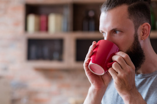 tea or coffee break and relaxing time concept. eating habits and energizing drink. bearded man having a cup of hot beverage in red mug.