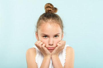 emotion face. frowning grumpy child with pursed lips and sad look. young cute girl portrait on blue background.