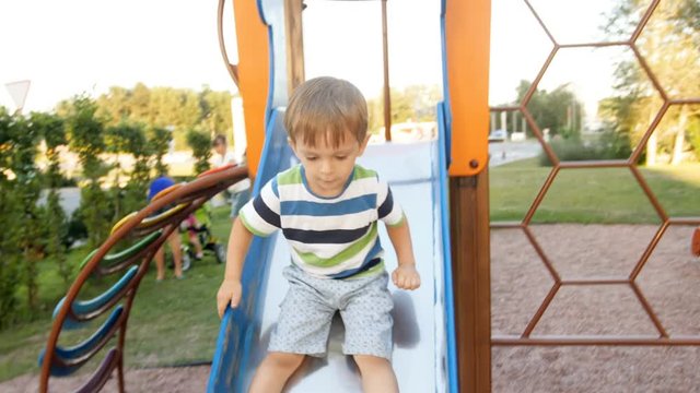 4k footage of little toddler boy riding on slide at playground at park
