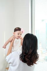 Mother and baby daughter happy and beautiful home together playing on the floor on window background