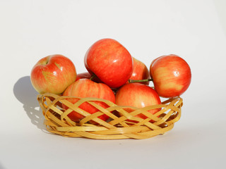 Apples red glossy in a wicker basket, isolated on white background.