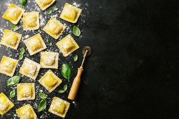 Raw ravioli with basil and flour on dark