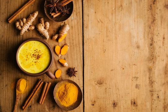 Hot turmeric milk with spices on wooden table