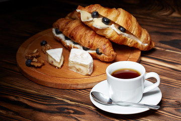 Cup of coffee with croissants, Camembert cheese, blueberries on a wooden background.