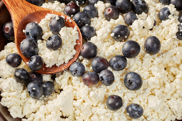 Cottage cheese with ripe blueberries in a clay bowl with a wooden spoon.