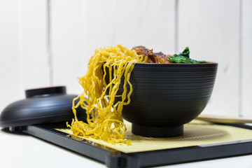 Noodle and duck in black cup on white wooden background,