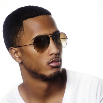 Portrait of a young black man wearing sunglasses against modern bright white background
