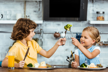 cute happy children holding forks with broccoli and having fun while eating together