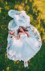 Beautiful, bride in a wedding dress lying at the grass. Wedding day. Bride posing on a green lawn....