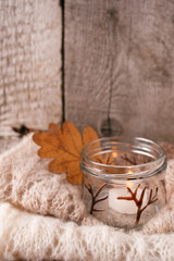 Obraz na płótnie Canvas warm sweater on wooden rustic bench, Candle, Quiet cozy homely scene. Fall autumn weekend. Monochrome concept, vertical, copy space