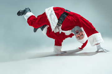 Funny serious guy with christmas hat dancing at studio. New Year Holiday. Christmas, x-mas, winter, gifts concept. Man wearing Santa Claus costume on gray. Copy space. Winter sales.