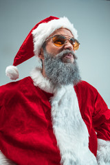 Funny serious guy with christmas hat posing at studio. New Year Holiday. Christmas, x-mas, winter, gifts concept. Man wearing Santa Claus costume on gray. Copy space. Winter sales.
