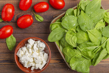 Fresh spinach leaves, feta cheese, tomatoes and spices on a dark wooden table