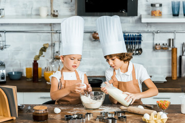 adorable kids in chef hats and aprons preparing dough for cookies in kitchen