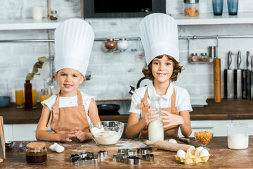 cute little children in chef hats and aprons preparing dough for cookies and smiling at camera