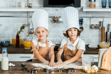 adorable children in aprons and chef hats preparing dough for tasty cookies together