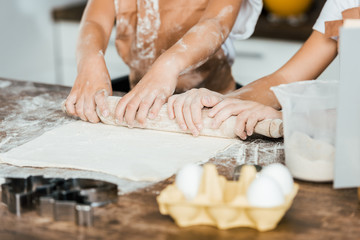 partial view of children holding rolling pin and preparing dough for delicious cookies
