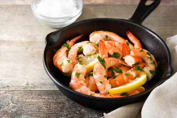 Grilled shrimps, parsley and lemon in iron pan on wooden table