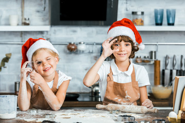 adorable kids in santa hats preparing christmas cookies and smiling at camera