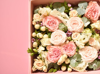 bouquet of small pink and peach roses with greens in a gift box on a pink background