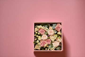 Obraz na płótnie Canvas bouquet of small pink and peach roses with greens in a gift box on a pink background