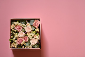 bouquet of small pink and peach roses with greens in a gift box on a pink background