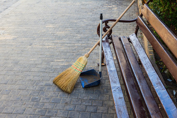  street cleaning - broom and scoop at the wooden bench on the sidewalk