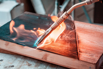 Artisan and carpenter burning wood planks, focus on the gas burner pistol, made of brass and orange rubber cable.