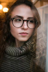 Warm, wintery portrait of young adult, female, gazing out the window with drops of water and bokeh