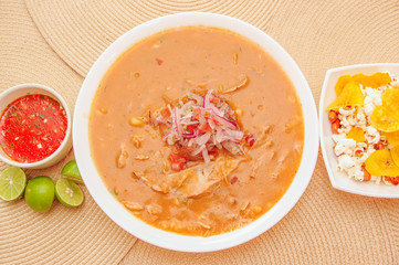 Above view of traditional Ecuadorian food called Encebollado, fish stew and ring onions inside, served with popcorn, chifles, lemon and red sauce inside of bowl