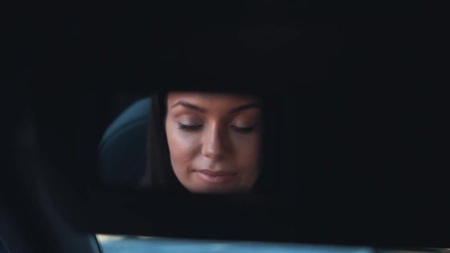 Attractive young woman applying lipstick in her car looking in mirror