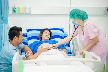 healthcare and people concept - close up of obstetrician doctor with stethoscope listening to pregnant woman baby heartbeat at hospital