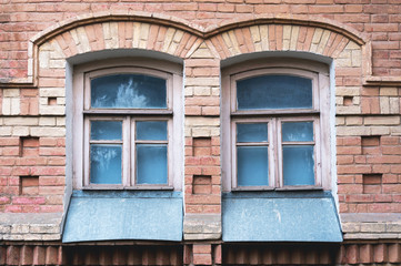 Fototapeta na wymiar Two vintage arched windows in a wall of yellow bricks. Green - the colors of sea wave glass in a maroon dark red wooden frame. The concept of antique vintage architecture in building elements