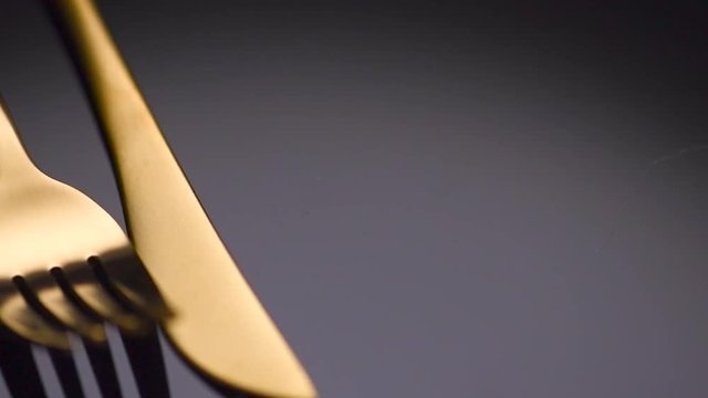 Luxury golden cutlery closeup. Knife and fork over black background. Rotation 360 degrees. 4K UHD video 3840x2160