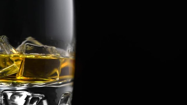 Whisky on the rocks. Glass of whiskey with ice isolated on black background. Rotation 360 degrees. 4K UHD video 3840x2160
