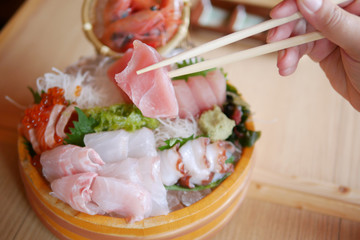 A piece of sliced japanese fish is tong by chopsticks selective focus over sashimi set