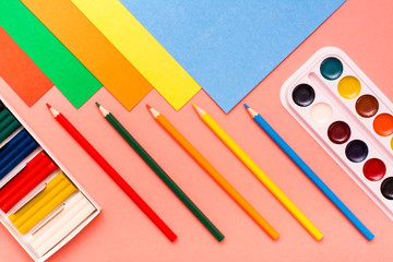 Items for creativity - sheets of colored cardboard, colored pencils, plasticine and watercolor on a red background. Top View