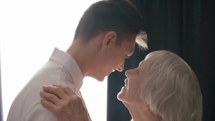 Tilt down medium shot of caring grandmother talking to grandson or son, hugging and kissing him, side view - Powered by Adobe