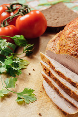 A filet of cold boiled turkey lies on a wooden board and vegetables with bread beside