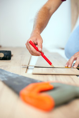 Young man measuring and marking laminate floor tile for cutting, installing laminate flooring. Close-up photo with focus on his hands. Home improvement and renovation concept