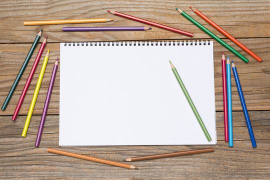 Blank page of a sketchbook with colored pencils on an old wooden table