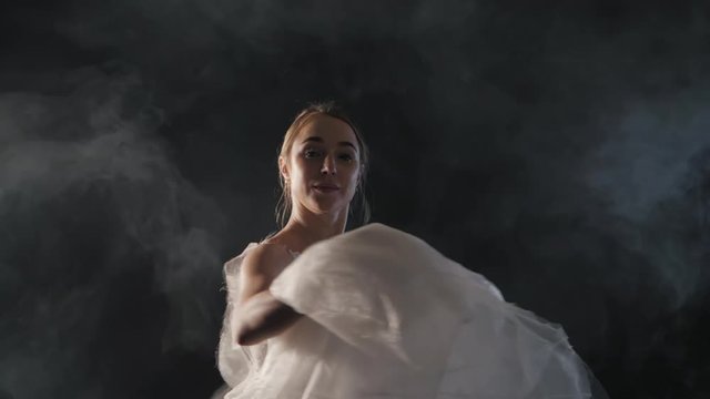 graceful ballerina doing a workout in the classroom. Smoke, fog, ballet dancer in white tutu, girl in pointe, whirls around in the dark with light on the black background, 4k