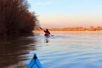 Man paddles a red kayak on the river or lake in fall season. Autumn kayaking