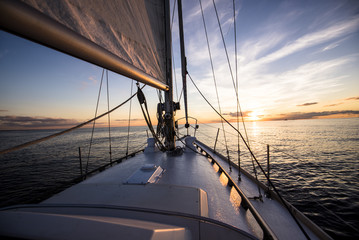 Obraz premium Sailing at sunset. A view from the yacht's deck to the bow and sails, Baltic sea, Latvia