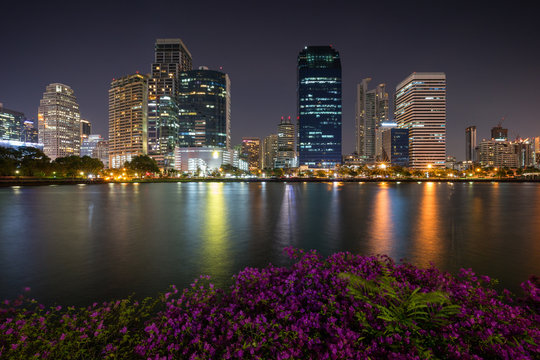 Scenic view of flowerbeds and lake at the Benjakiti (Benjakitti) Park and lit skyscrapers in Bangkok, Thailand, in the evening.